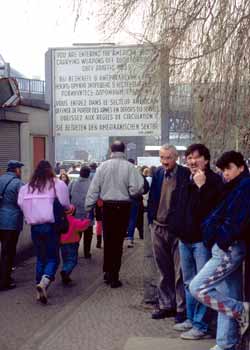 People walking past sign that says 'You Are Entering American Sector' in English, French, German and Russian.